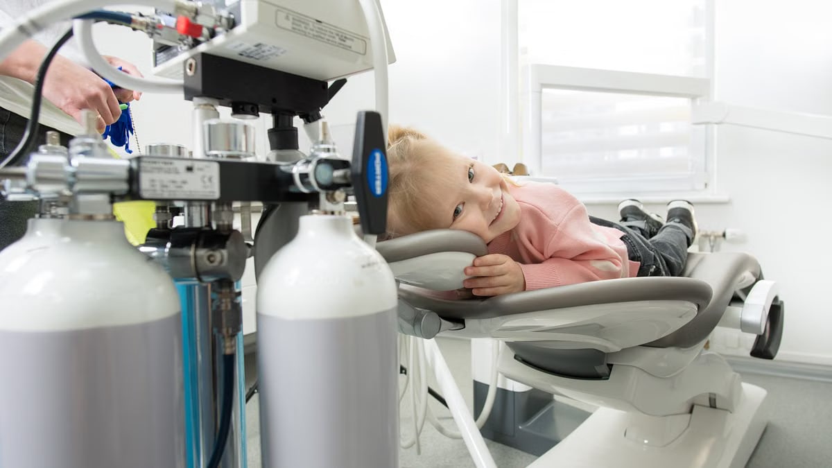 Smiling child lying on a dental chair during a checkup in a dental clinic with equipment in view.